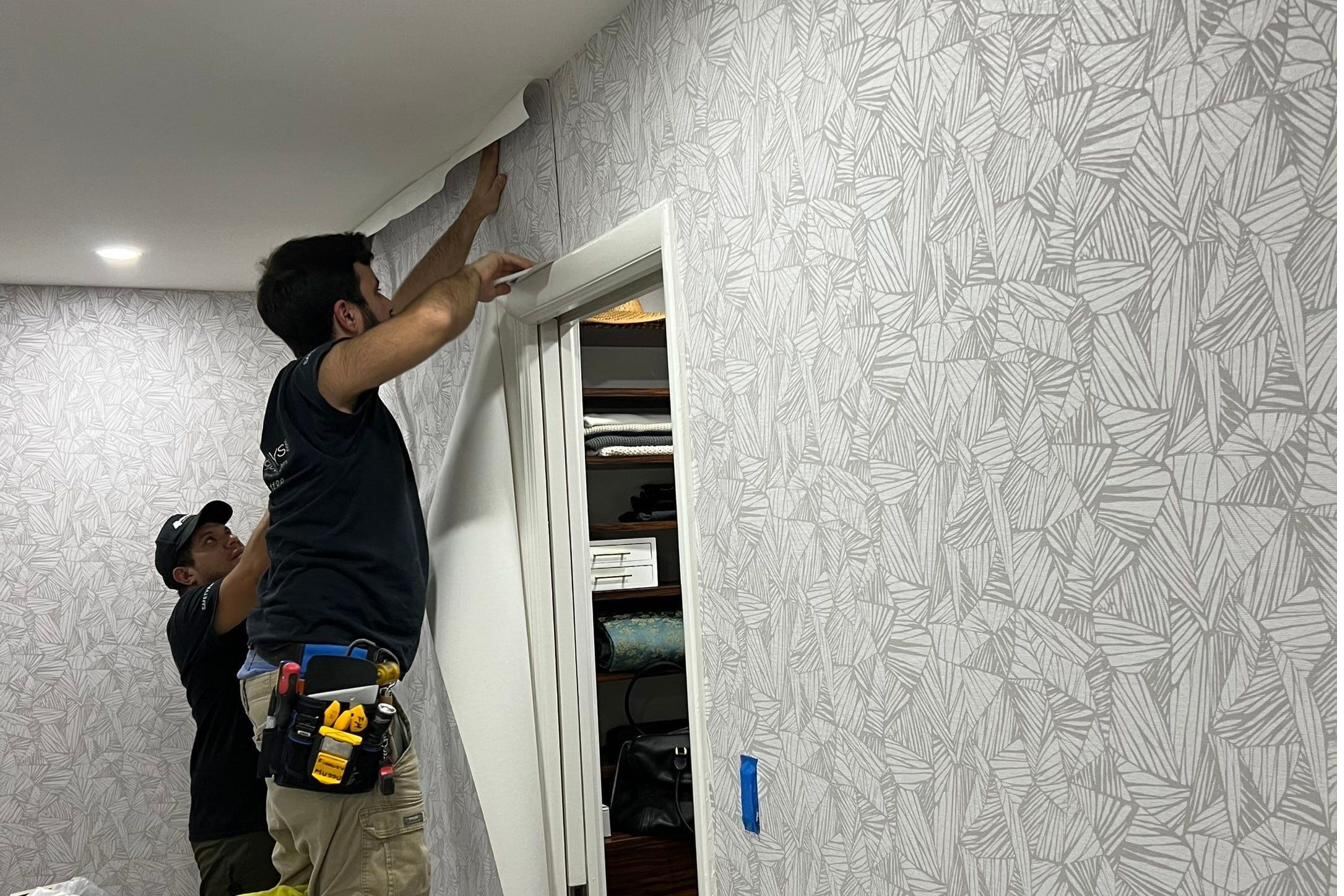 Two-person wallpaper installation team applying customised wallpaper to a wall — professional installation by Siddhi Decorators, Pitampura